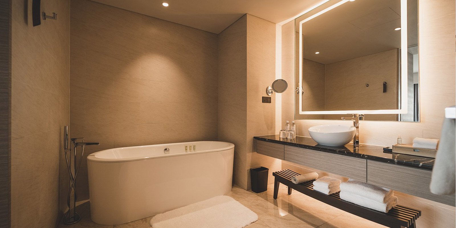 Ein modernes Badezimmer mit einer freistehenden Badewanne, eleganten Fliesen und einem stilvollen Waschbecken auf einem Holzregal.