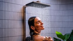Eine Frau genießt eine erfrischende Dusche, während Wasser sanft über ihr Gesicht fließt und sie entspannt lächelt.
