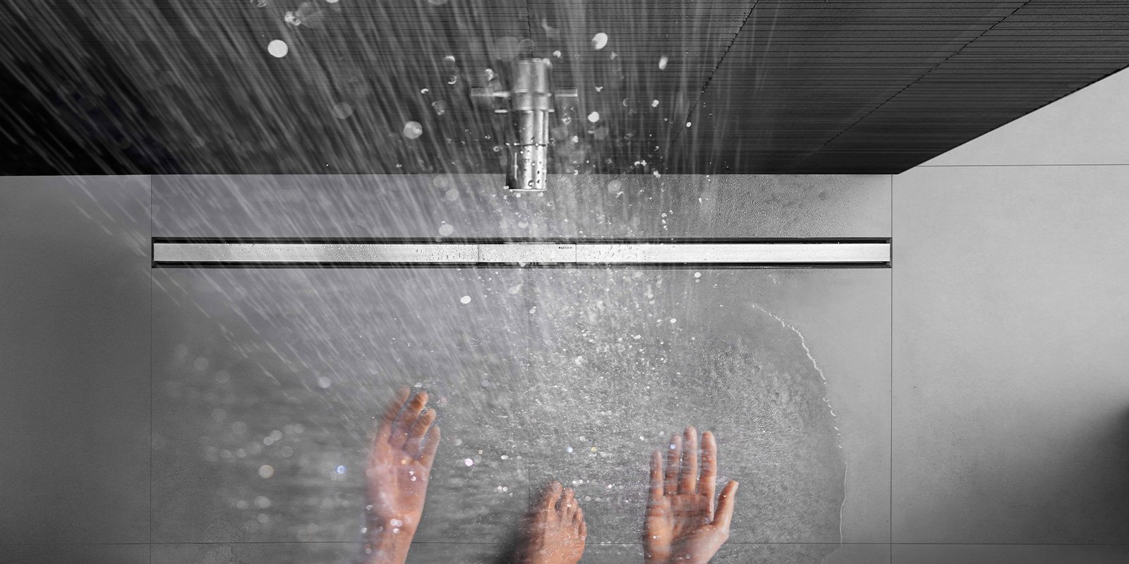 Wassertropfen fallen sanft auf die Hände, die unter einer modernen Dusche stehen, während der Boden nass wird.