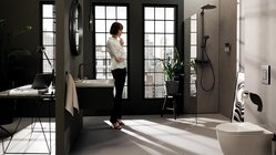 Eine Frau steht nachdenklich in einem modernen Badezimmer mit großen Fenstern und Blick auf die Stadt.