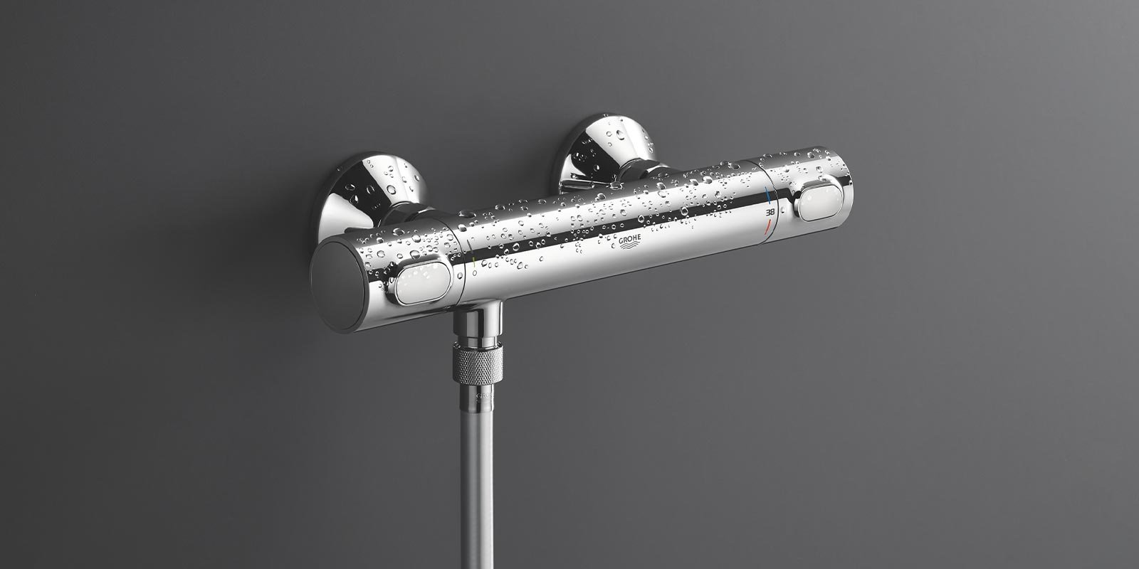 Ein glänzender, chromfarbener Duschthermostat mit Wassertropfen, montiert an einer grauen Wand.