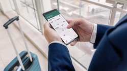 Eine Person in einem Anzug hält ein Smartphone und überprüft die Temperatur und Luftfeuchtigkeit in einem modernen Raum.